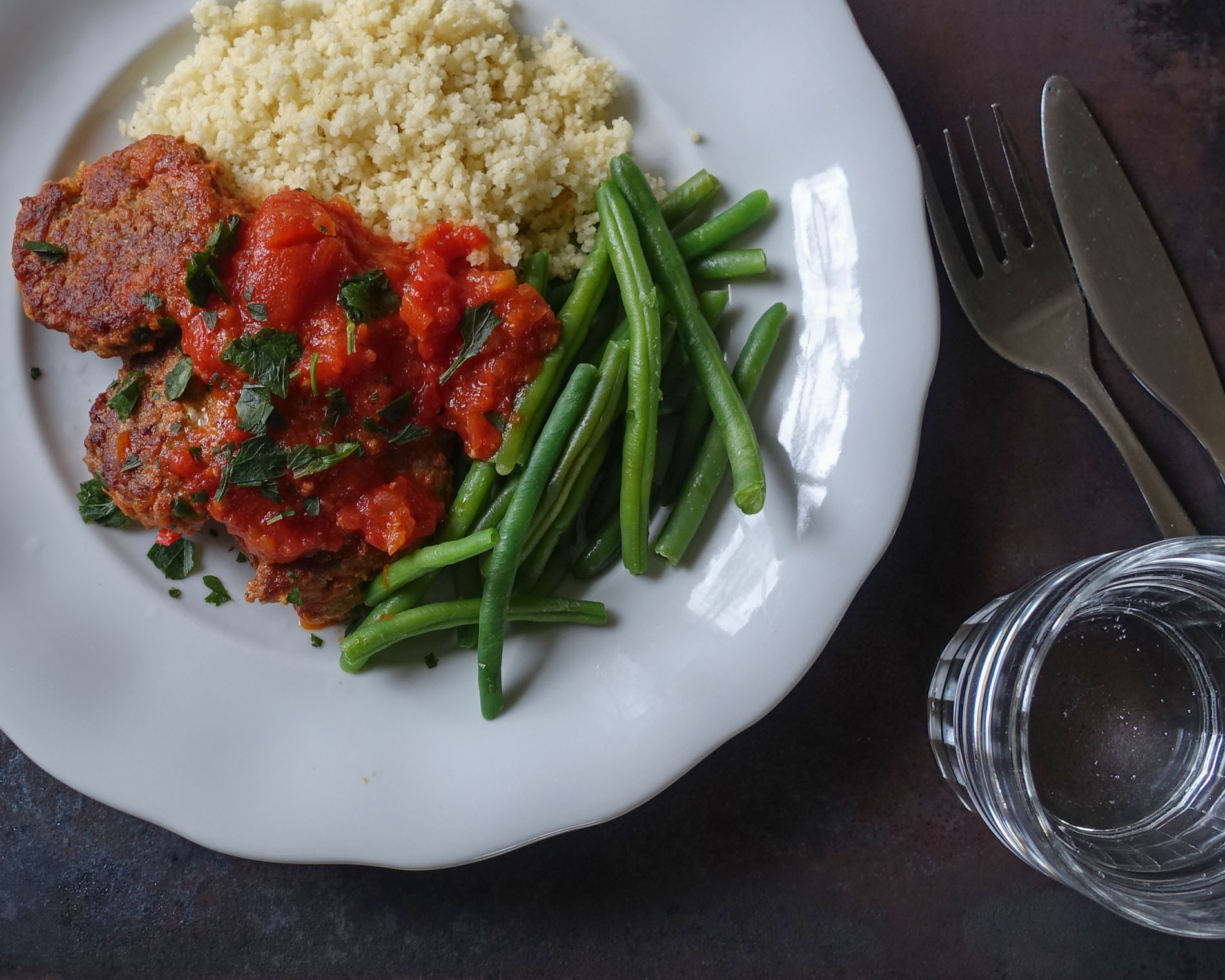 köttfärsbiffar med tomatsås och couscous på en vit tallrik